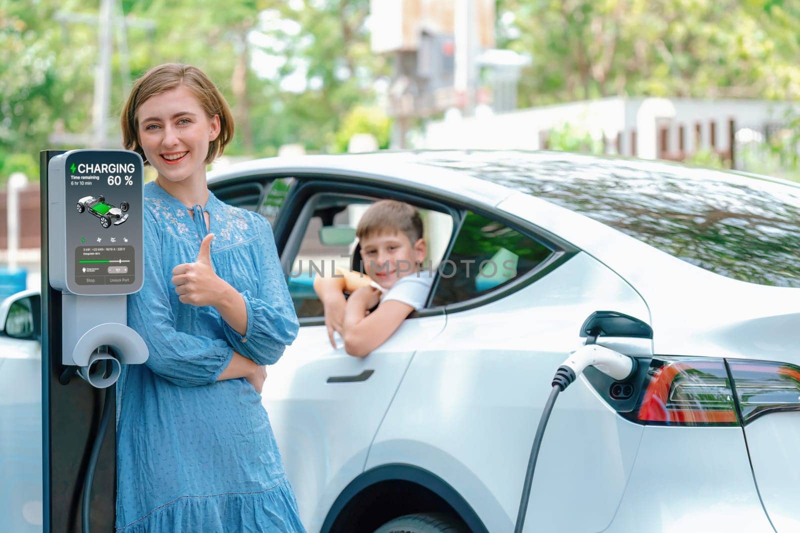 Environmental awareness family with eco-friendly electric car recharging battery from home EV charging station with little boy inside the car. Rechargeable and EV car technology. Perpetual