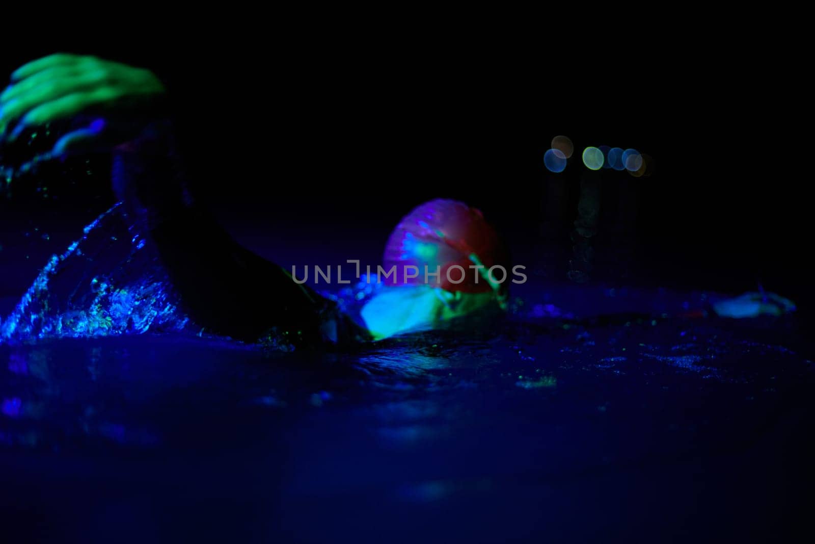 Real triathlete swimmer having a break during hard training at lake on dark night neon gel color lights