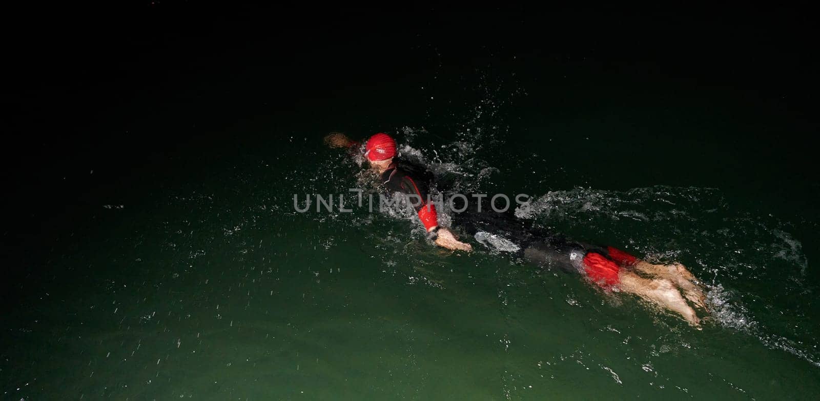 A determined professional triathlete undergoes rigorous night time training in cold waters, showcasing dedication and resilience in preparation for an upcoming triathlon swim competition by dotshock