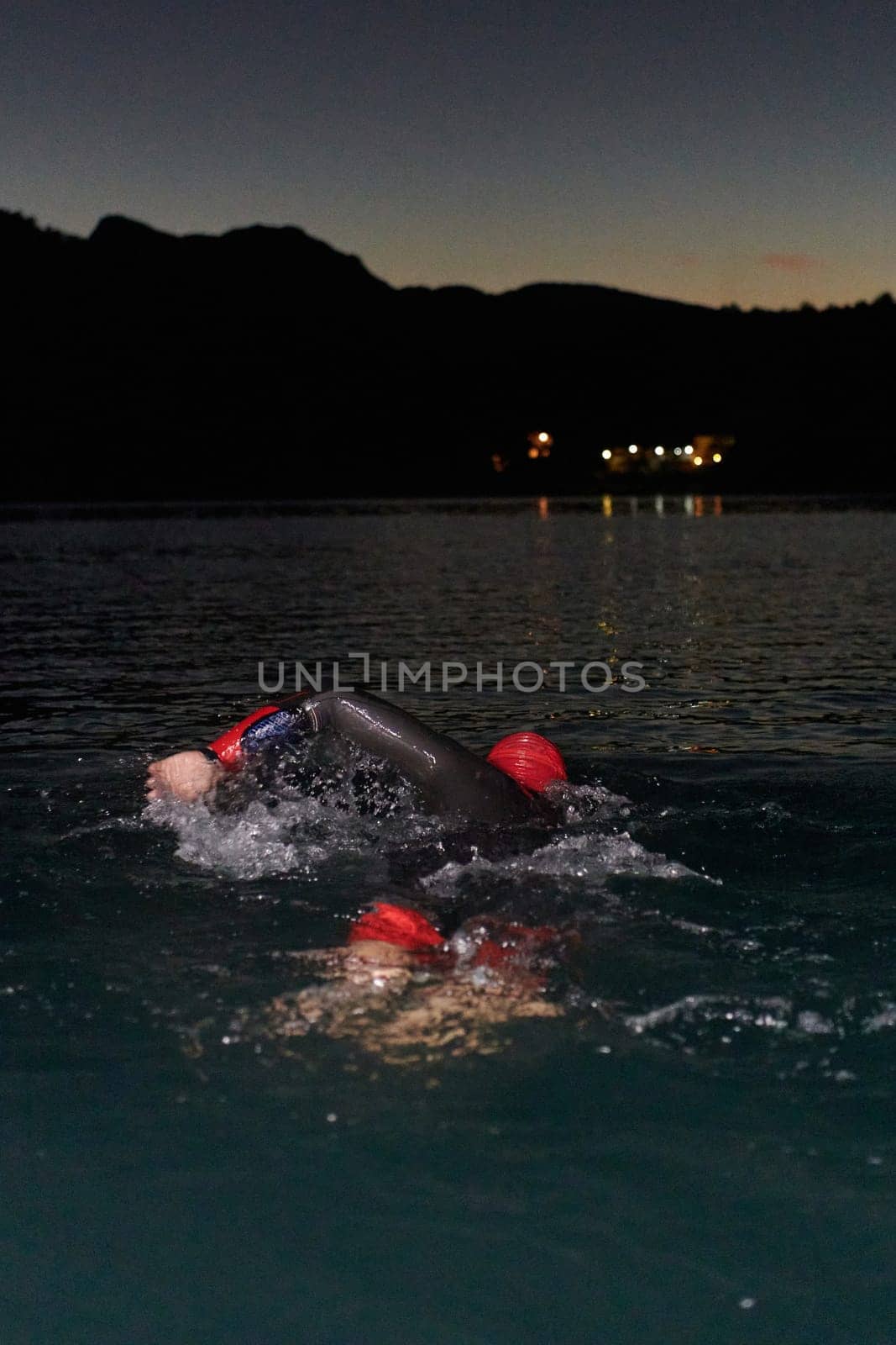 A determined professional triathlete undergoes rigorous night time training in cold waters, showcasing dedication and resilience in preparation for an upcoming triathlon swim competition by dotshock