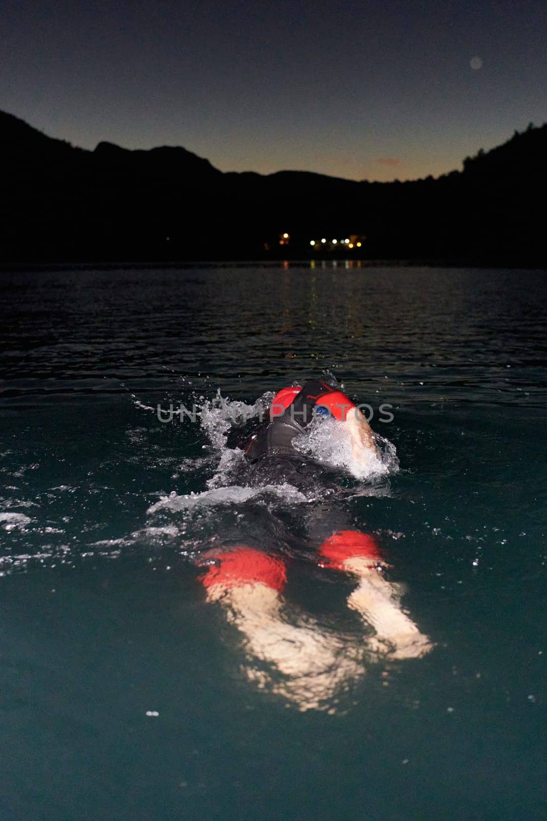 A determined professional triathlete undergoes rigorous night time training in cold waters, showcasing dedication and resilience in preparation for an upcoming triathlon swim competition by dotshock