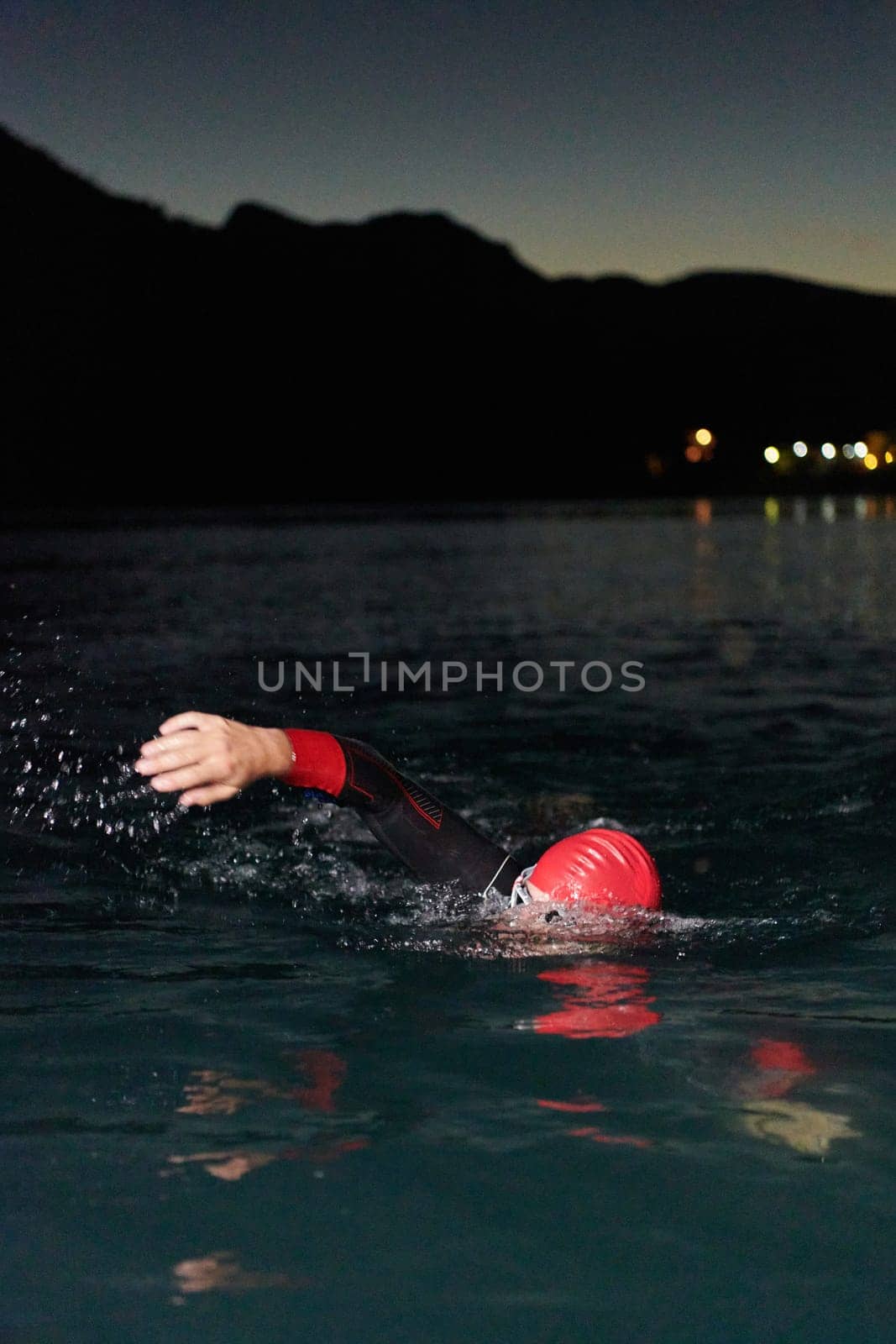 A determined professional triathlete undergoes rigorous night time training in cold waters, showcasing dedication and resilience in preparation for an upcoming triathlon swim competition.