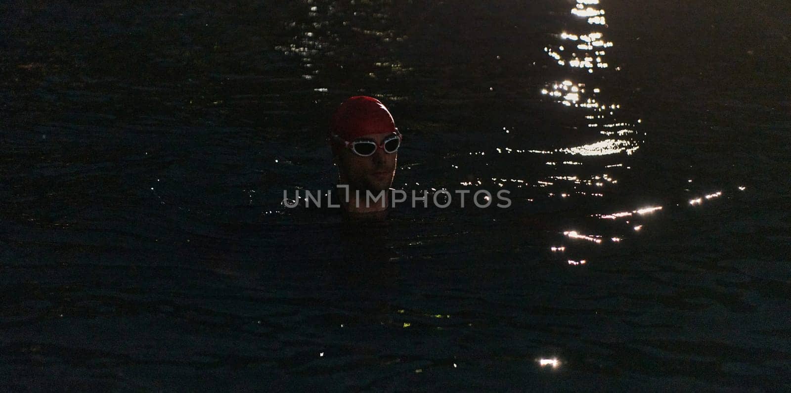 A determined professional triathlete undergoes rigorous night time training in cold waters, showcasing dedication and resilience in preparation for an upcoming triathlon swim competition by dotshock