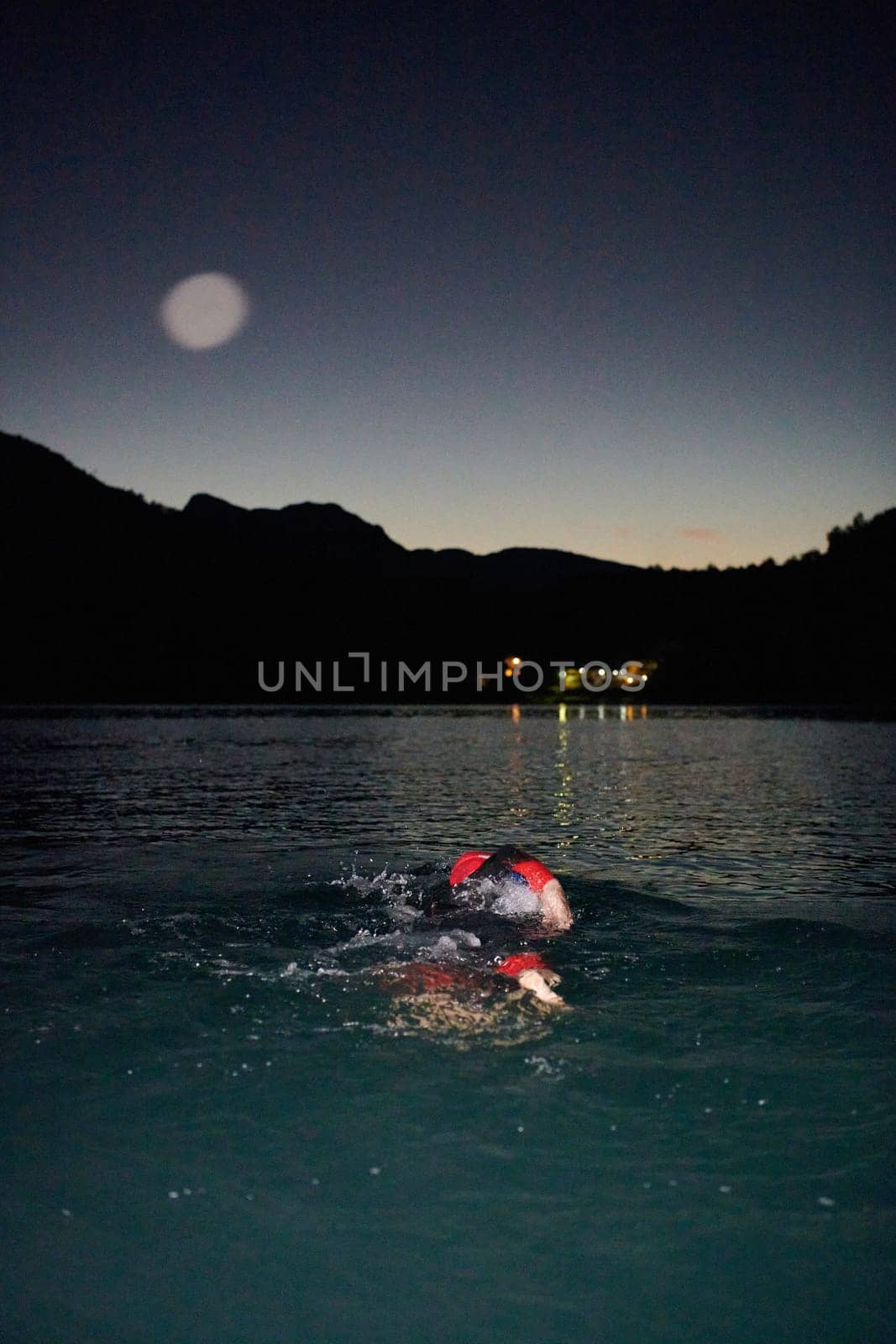 A determined professional triathlete undergoes rigorous night time training in cold waters, showcasing dedication and resilience in preparation for an upcoming triathlon swim competition.