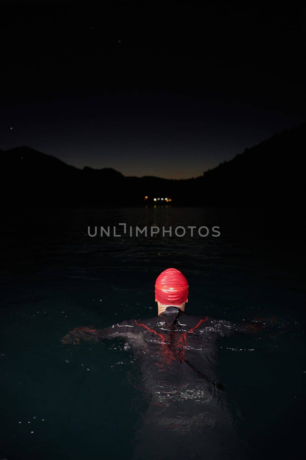 A determined professional triathlete undergoes rigorous night time training in cold waters, showcasing dedication and resilience in preparation for an upcoming triathlon swim competition.