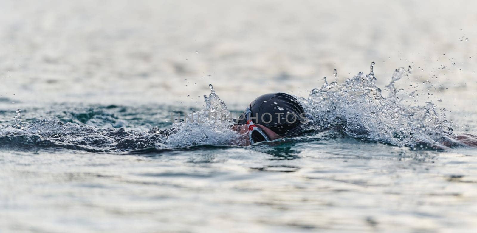 A professional triathlete trains with unwavering dedication for an upcoming competition at a lake, emanating a sense of athleticism and profound commitment to excellence. by dotshock