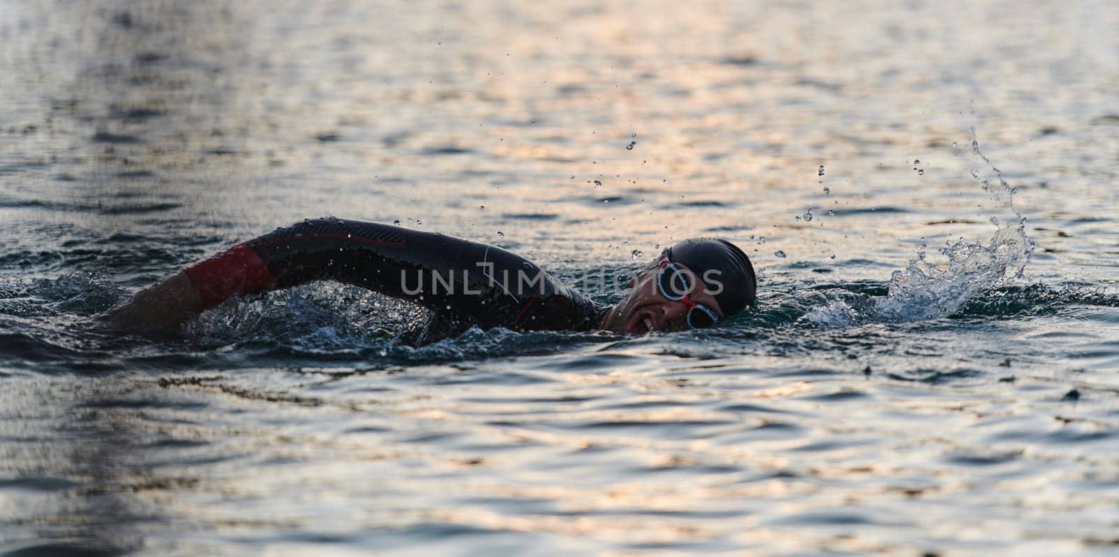 A professional triathlete trains with unwavering dedication for an upcoming competition at a lake, emanating a sense of athleticism and profound commitment to excellence. by dotshock