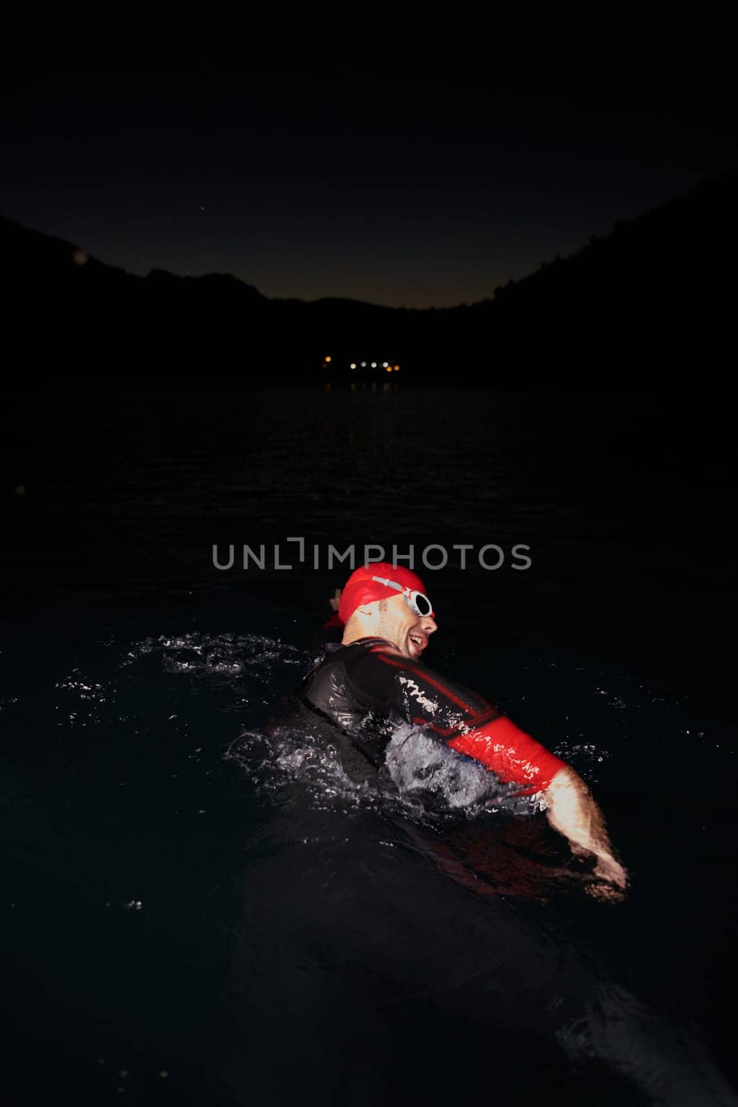 A determined professional triathlete undergoes rigorous night time training in cold waters, showcasing dedication and resilience in preparation for an upcoming triathlon swim competition.