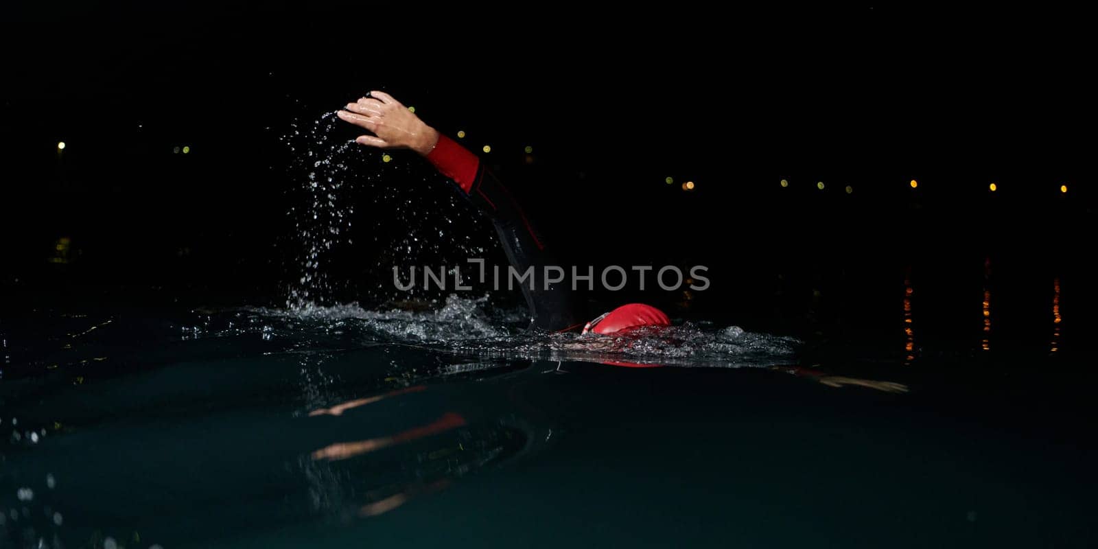 A determined professional triathlete undergoes rigorous night time training in cold waters, showcasing dedication and resilience in preparation for an upcoming triathlon swim competition.