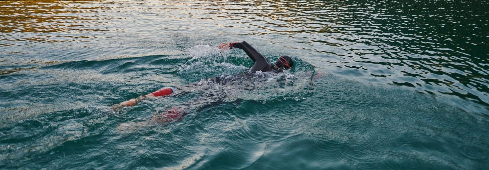 A professional triathlete trains with unwavering dedication for an upcoming competition at a lake, emanating a sense of athleticism and profound commitment to excellence. by dotshock