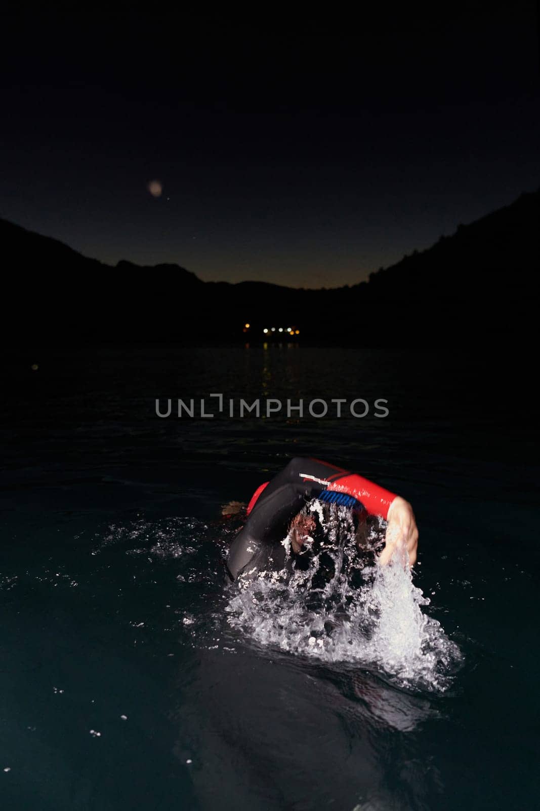 A determined professional triathlete undergoes rigorous night time training in cold waters, showcasing dedication and resilience in preparation for an upcoming triathlon swim competition.