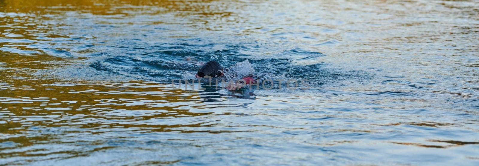 Triathlon athlete swimming on lake in sunrise wearing wetsuit by dotshock