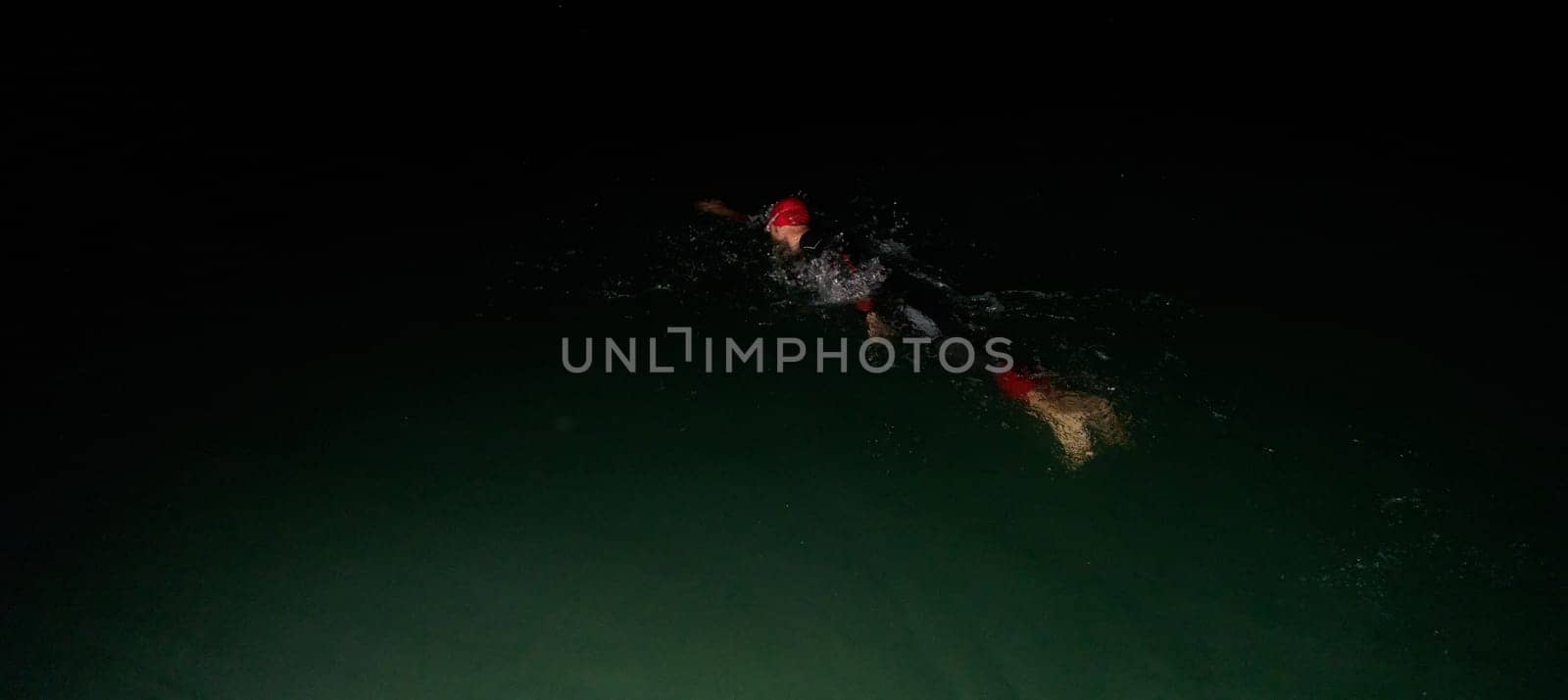 A determined professional triathlete undergoes rigorous night time training in cold waters, showcasing dedication and resilience in preparation for an upcoming triathlon swim competition by dotshock