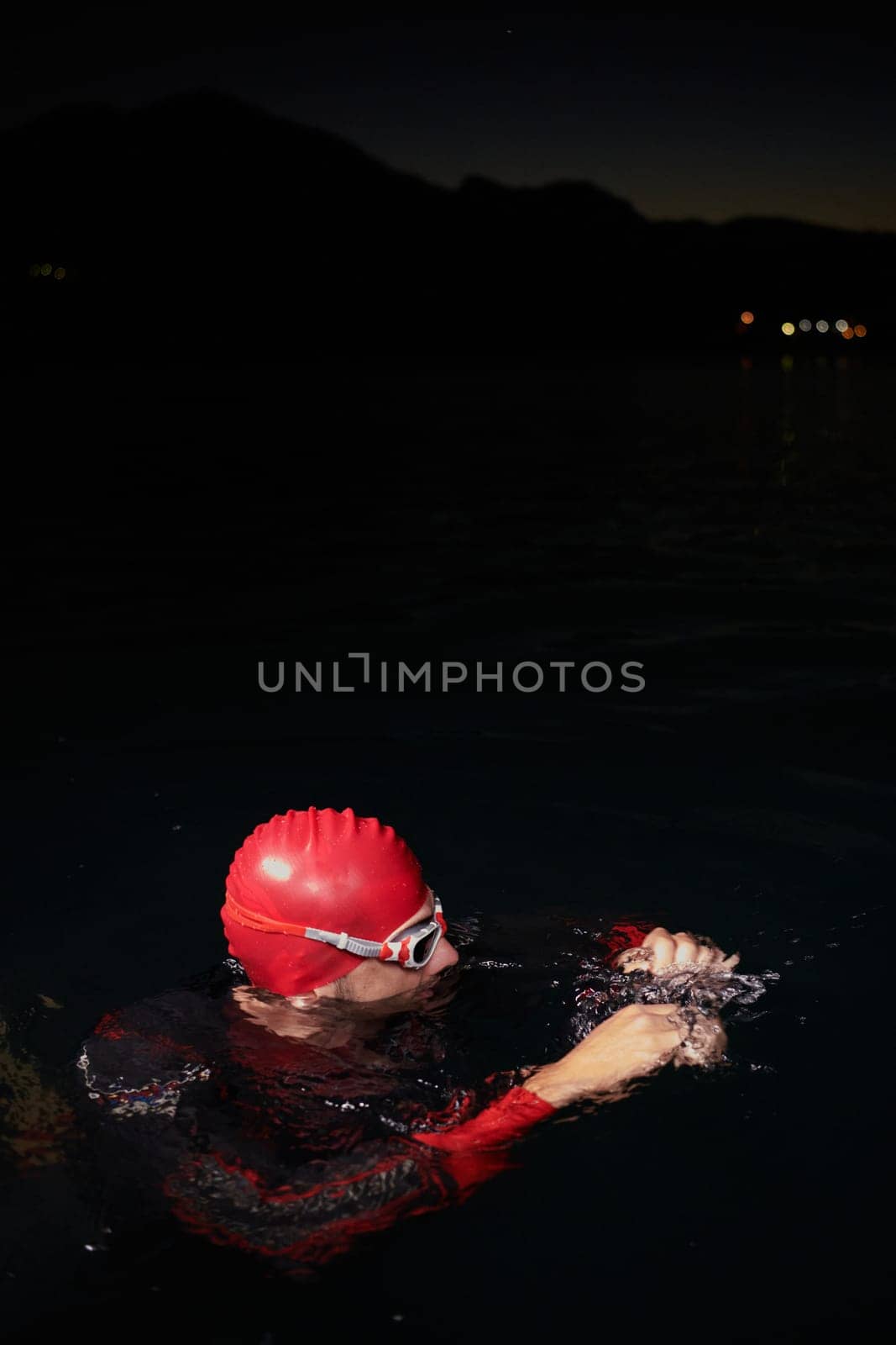 A determined professional triathlete undergoes rigorous night time training in cold waters, showcasing dedication and resilience in preparation for an upcoming triathlon swim competition by dotshock