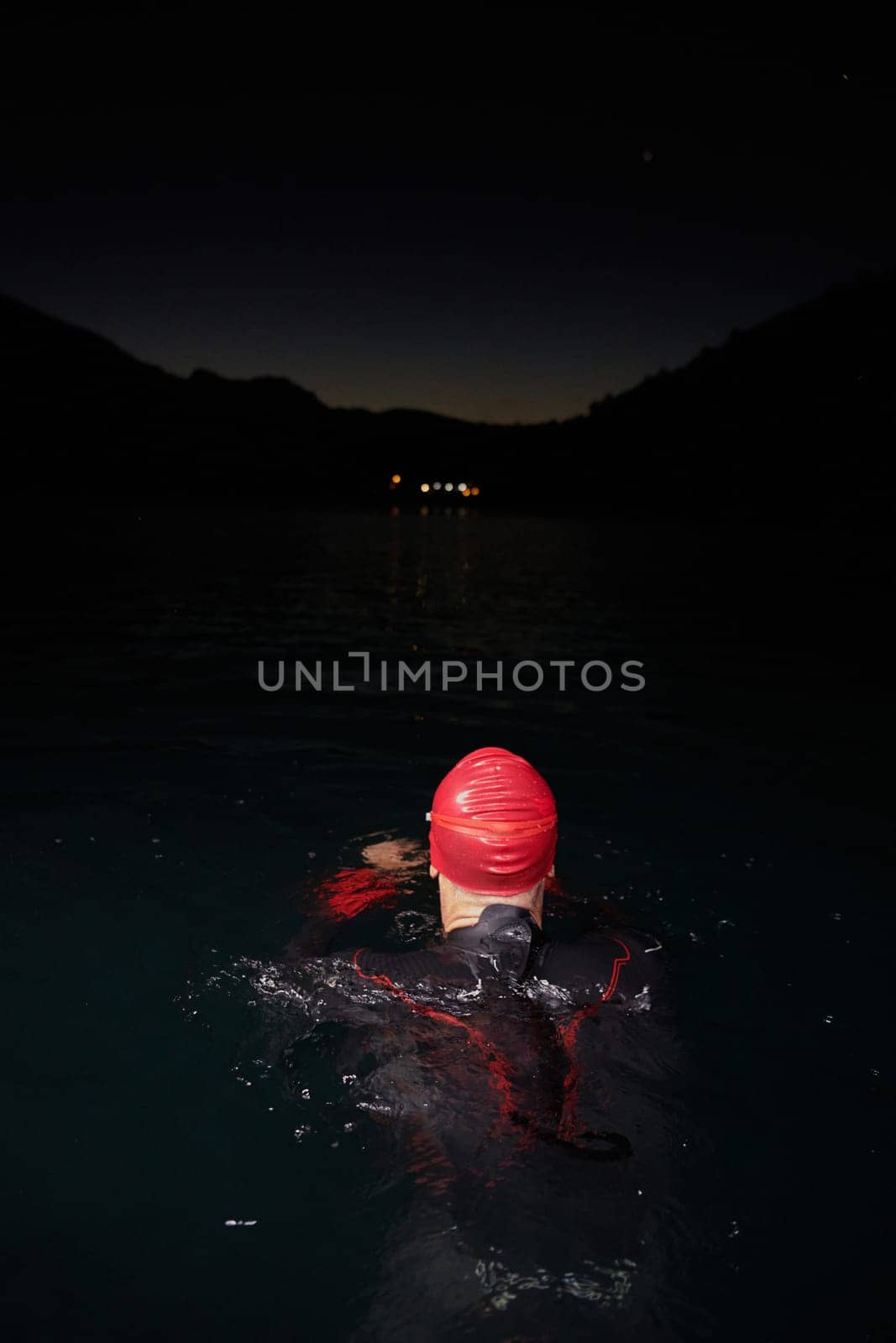 A determined professional triathlete undergoes rigorous night time training in cold waters, showcasing dedication and resilience in preparation for an upcoming triathlon swim competition.