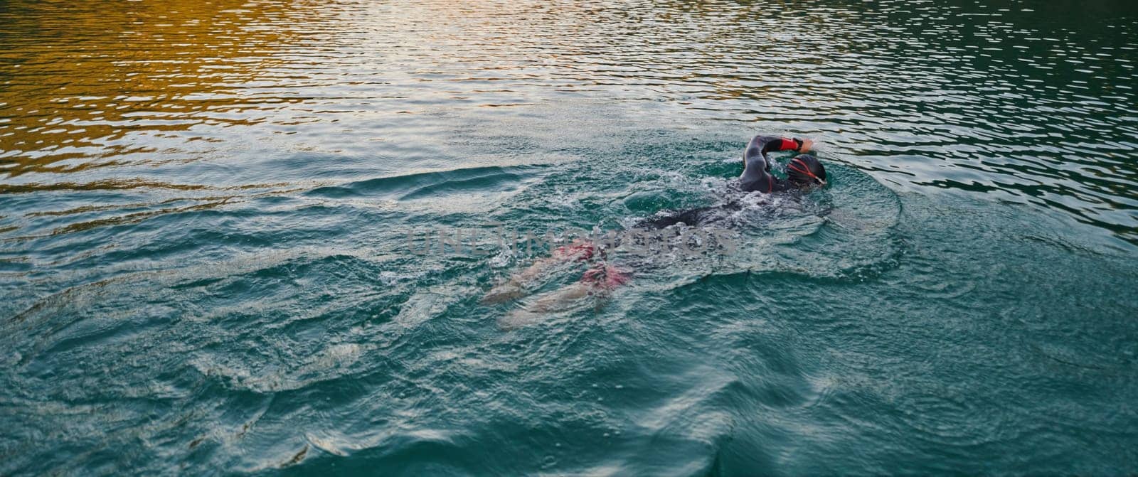 A professional triathlete trains with unwavering dedication for an upcoming competition at a lake, emanating a sense of athleticism and profound commitment to excellence. by dotshock