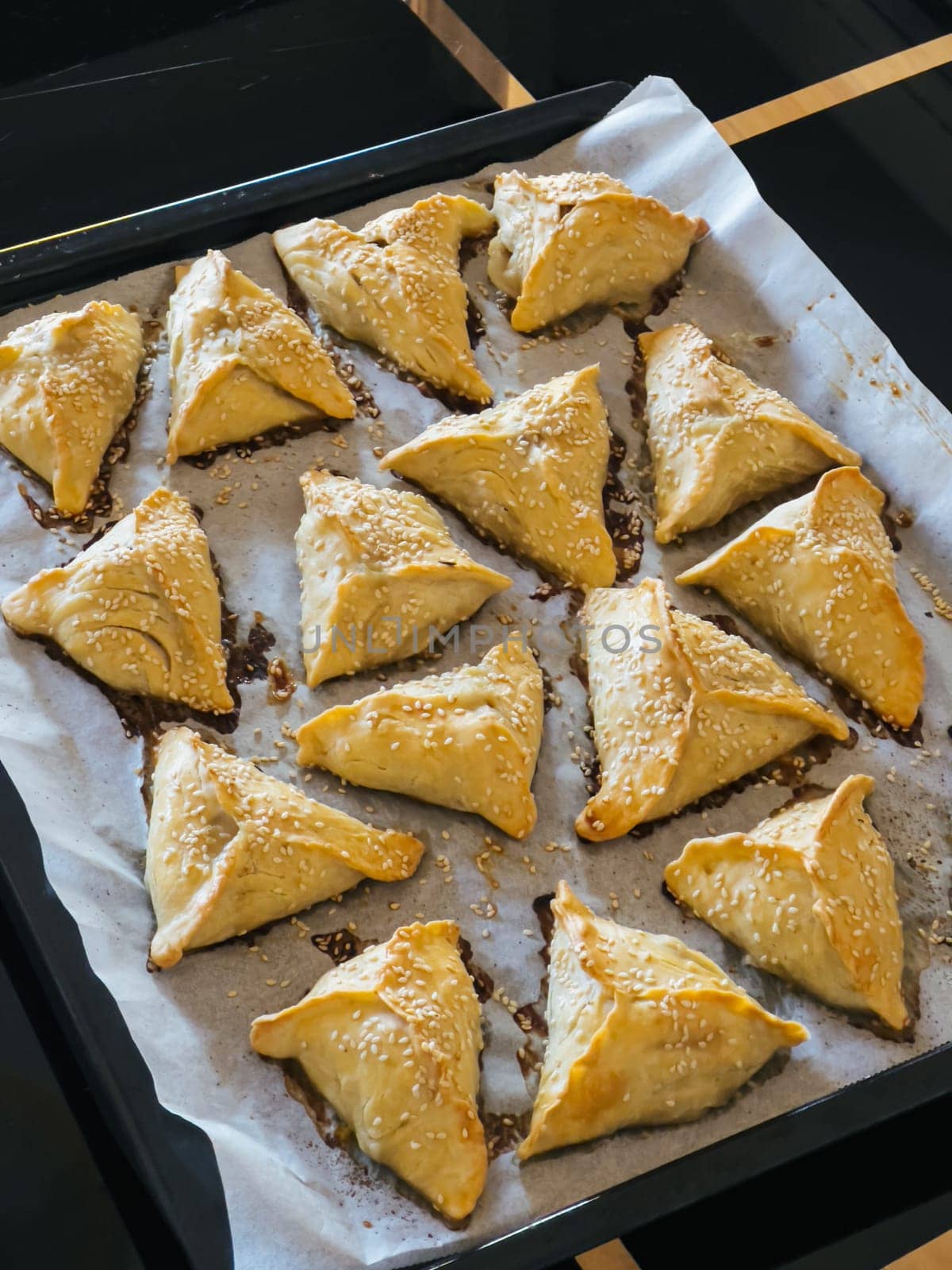 Triangular puff pastry pies with sesame seeds lie on a tray on the table. High quality photo