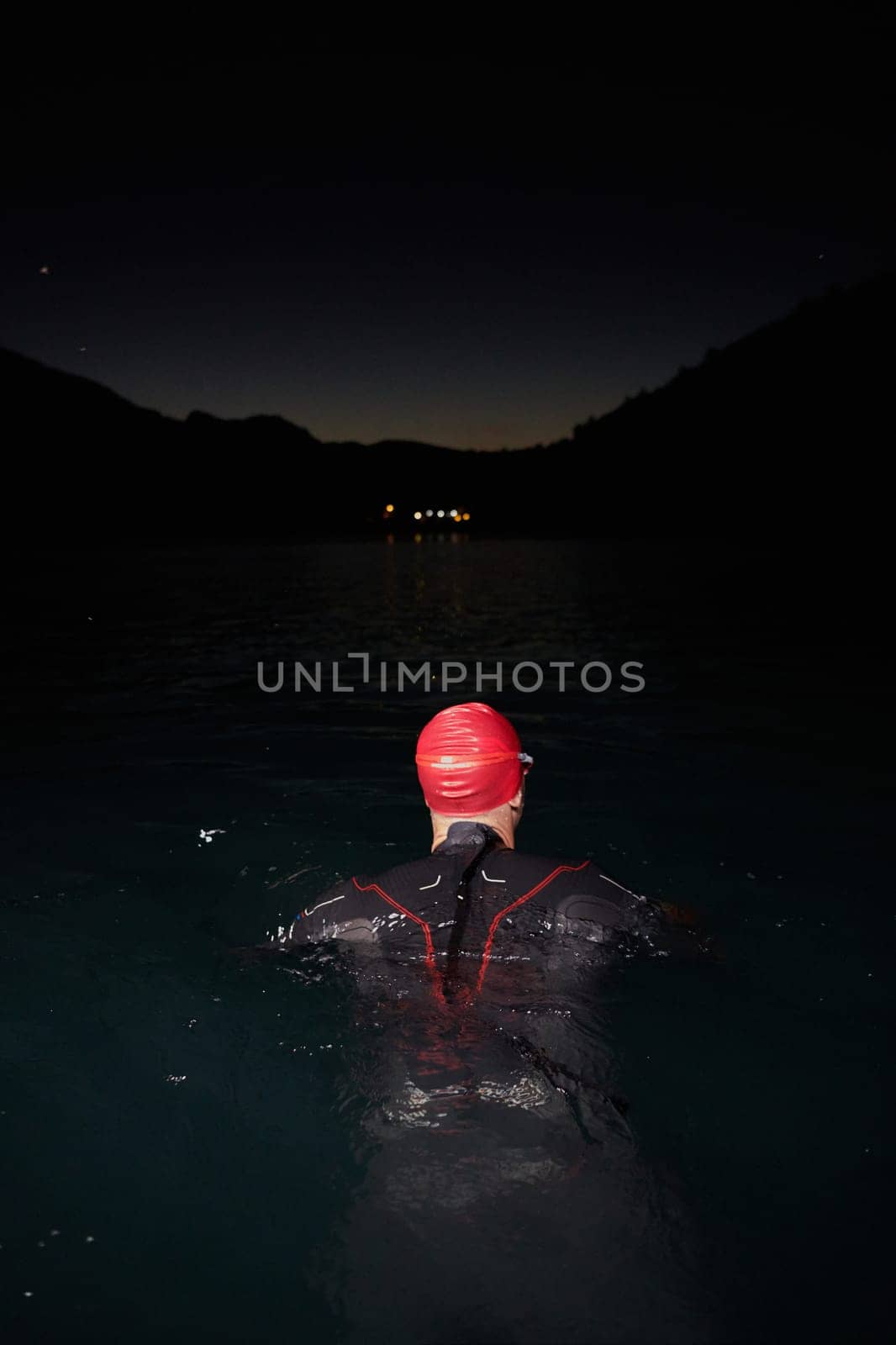 A determined professional triathlete undergoes rigorous night time training in cold waters, showcasing dedication and resilience in preparation for an upcoming triathlon swim competition.