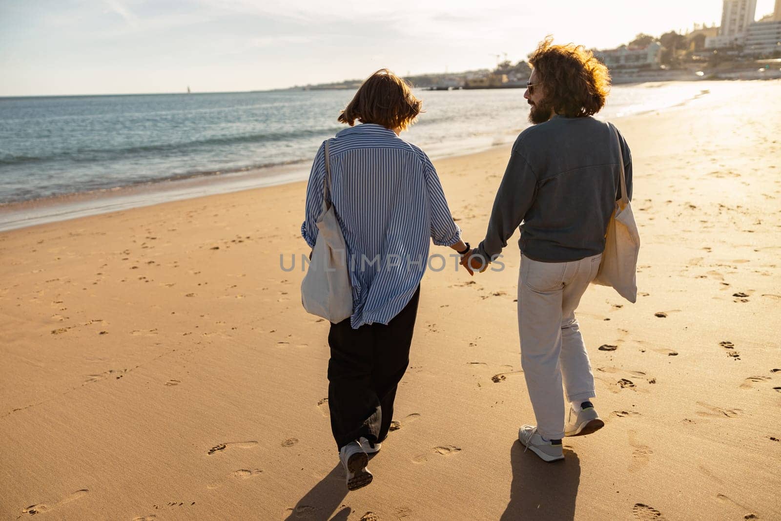 Rear view of couple in love is walk holding hands across the sunny beach. High quality photo