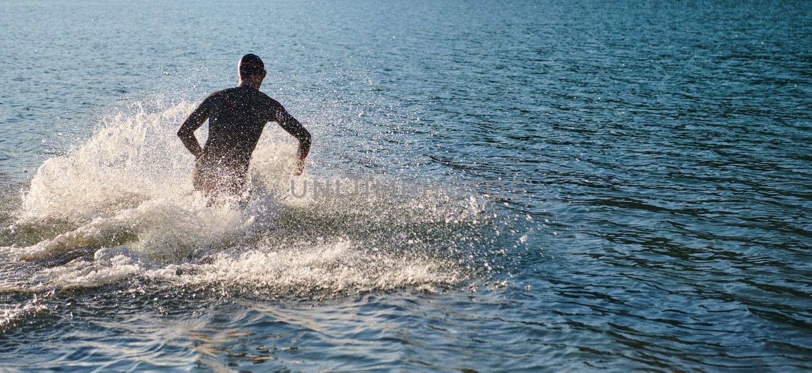 Triathlon athlete starting swimming training on lake by dotshock