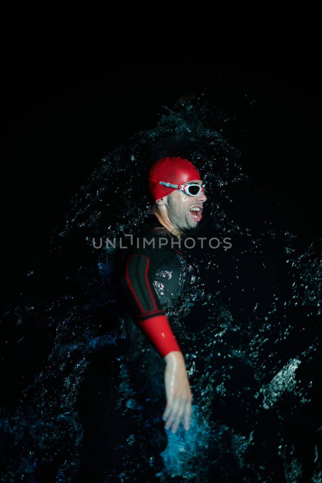 Real triathlete swimmer having a break during hard training at lake on dark night neon gel color lights