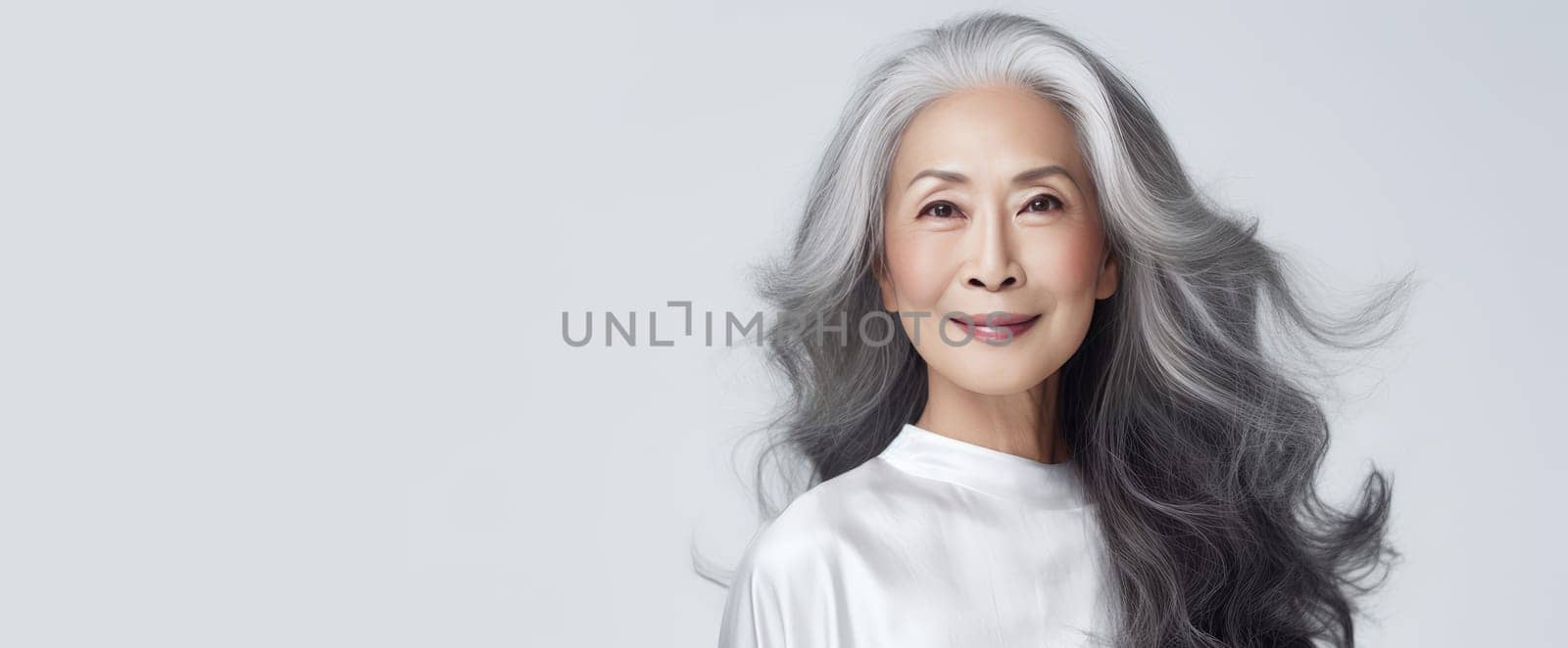 Smiling, elderly, chic Asian woman with gray long hair and perfect skin, on white background, banner. Advertising of cosmetic products, spa treatments, shampoos and hair care products, dentistry and medicine, perfumes and cosmetology for senior women