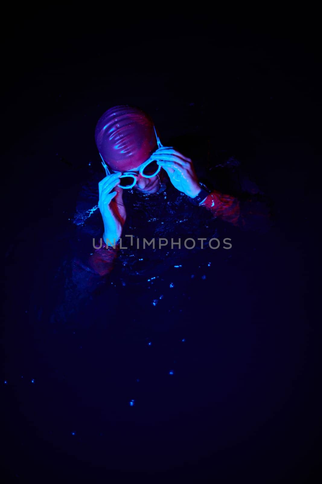 Real triathlete swimmer having a break during hard training at lake on dark night neon gel color lights