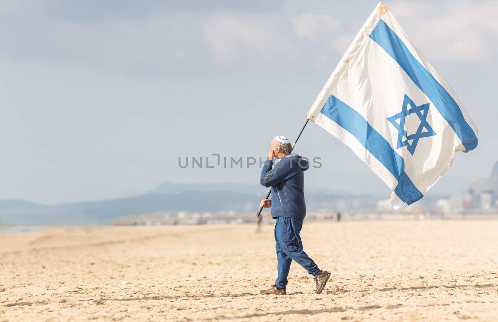 25 november 2023, Lisbon, Portugal - A Man Walking on a Beach Holding a Flag of Israel by Studia72