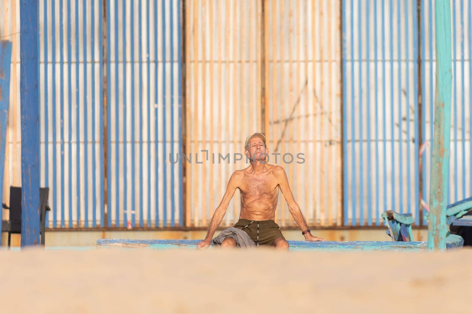 25 november 2023, Lisbon, Portugal - Shirtless Man Sitting on Surfboard in Sandy Beach by Studia72