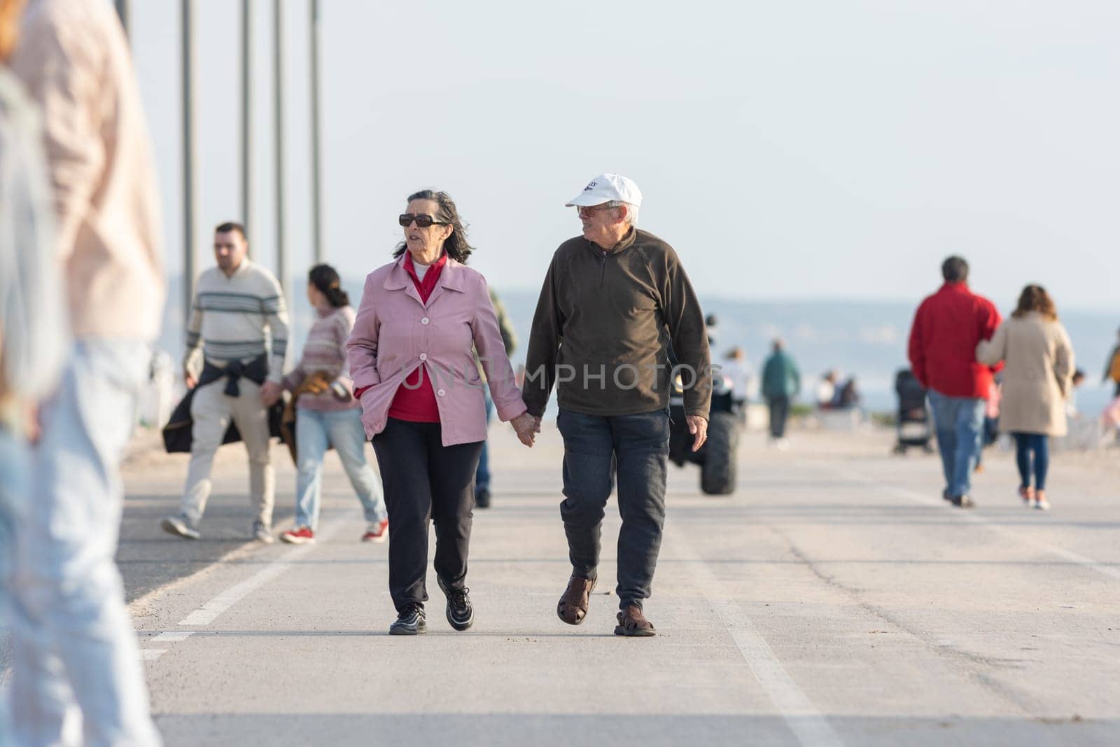 25 november 2023, Lisbon, Portugal - elderly Couple Holding Hands While Walking on promenade near ocean