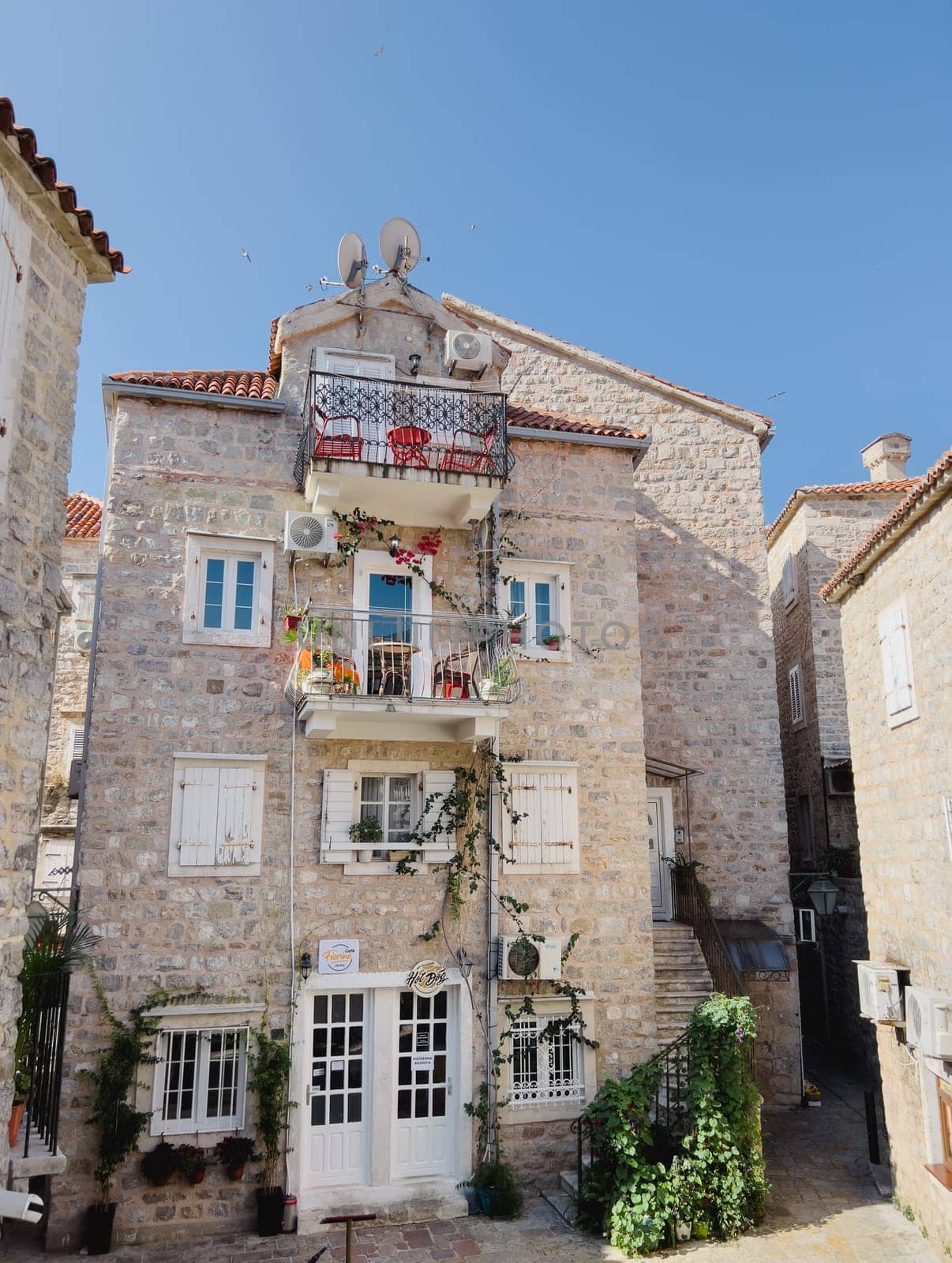 Budva, Montenegro - 08 august 2023: Old stone house with garlands of green plants on the balconies by Nadtochiy