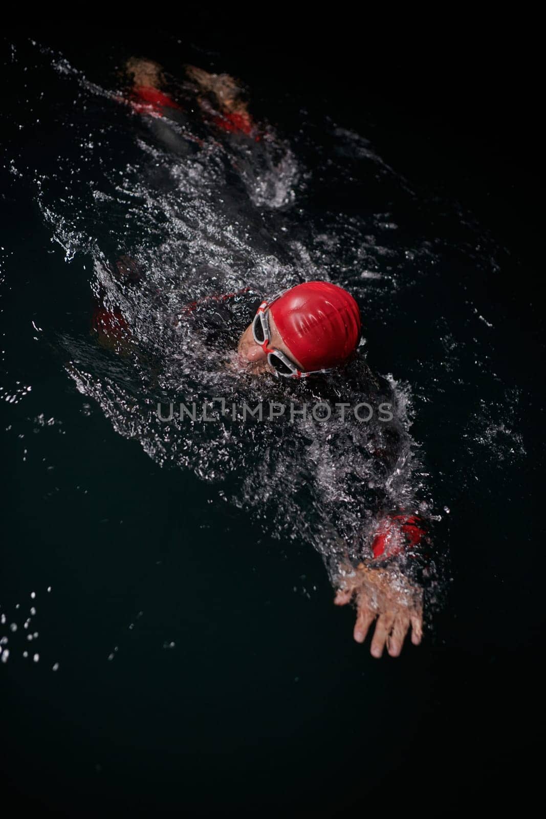 A determined professional triathlete undergoes rigorous night time training in cold waters, showcasing dedication and resilience in preparation for an upcoming triathlon swim competition by dotshock