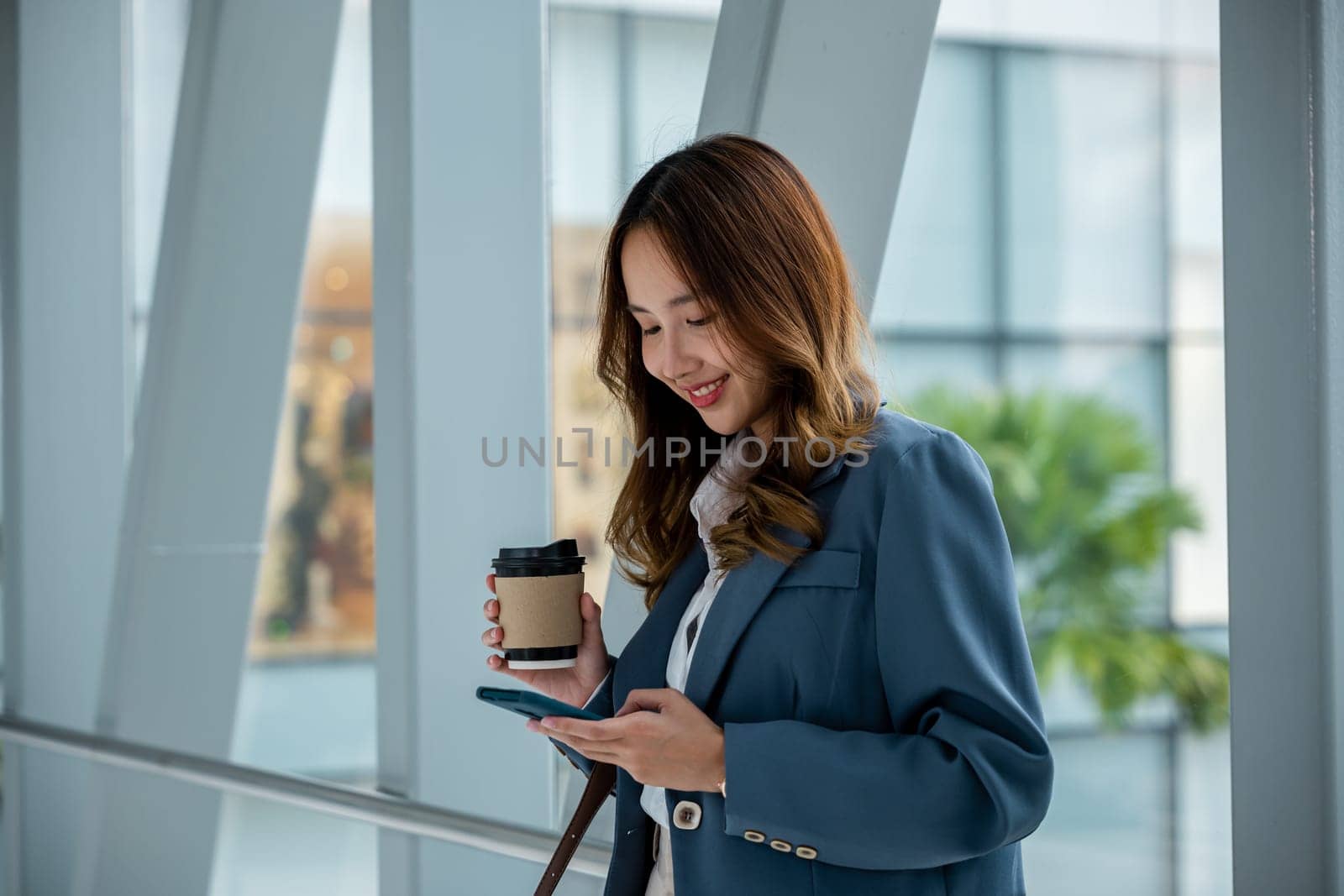 Smiling Asian woman with coffee and smartphone walking on escalator by Sorapop