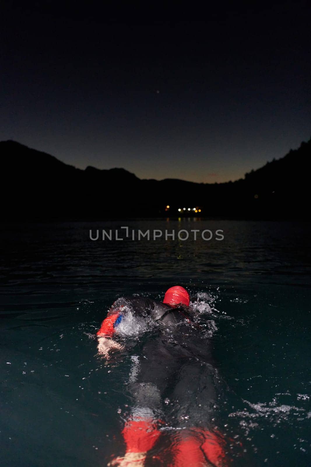 A determined professional triathlete undergoes rigorous night time training in cold waters, showcasing dedication and resilience in preparation for an upcoming triathlon swim competition.