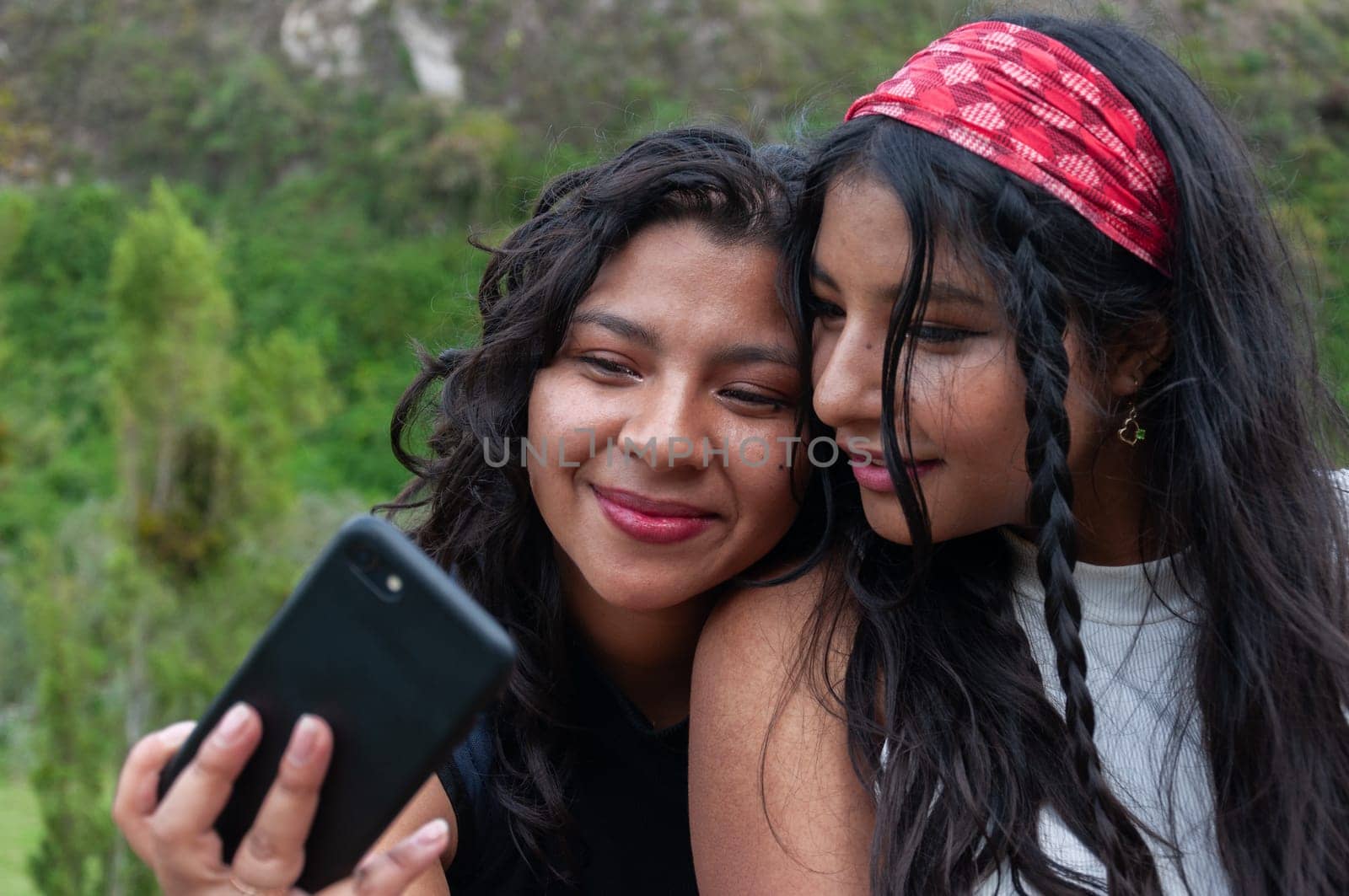 two Latina friends of generation Z looking at a cell phone with gratifying faces after seeing a photo. by Raulmartin