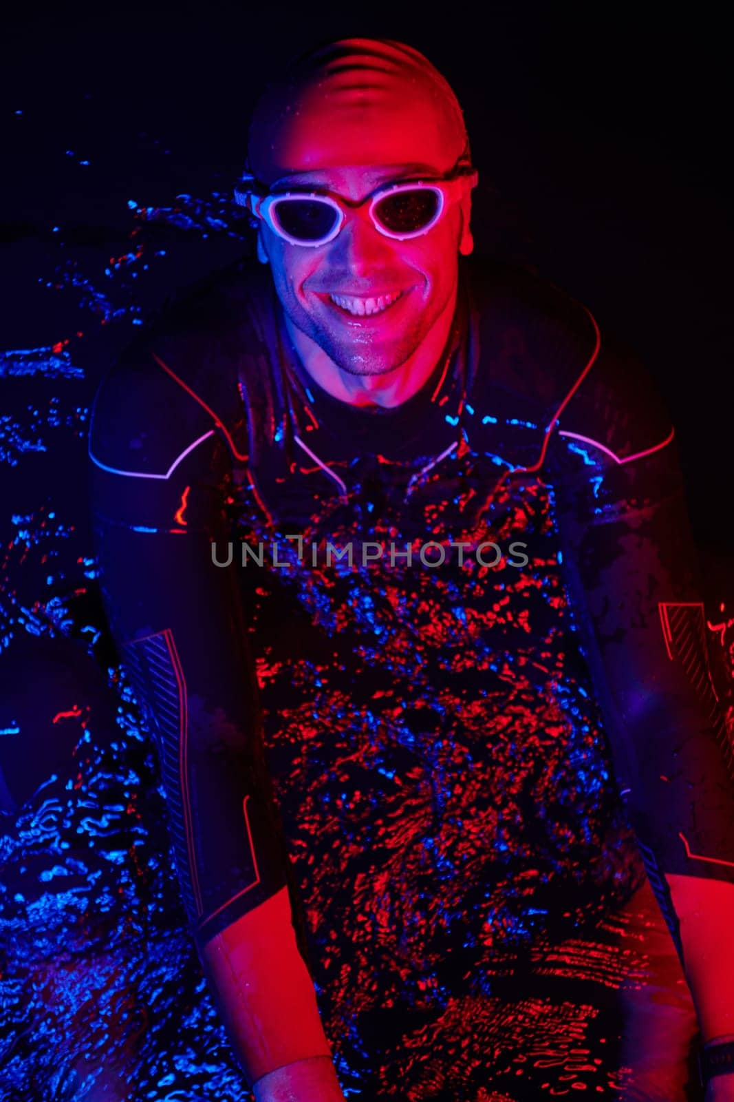 real triathlete swimmer having a break during hard training at lake on dark night neon gel color lights