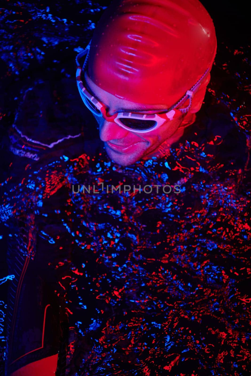 real triathlete swimmer having a break during hard training at lake on dark night neon gel color lights