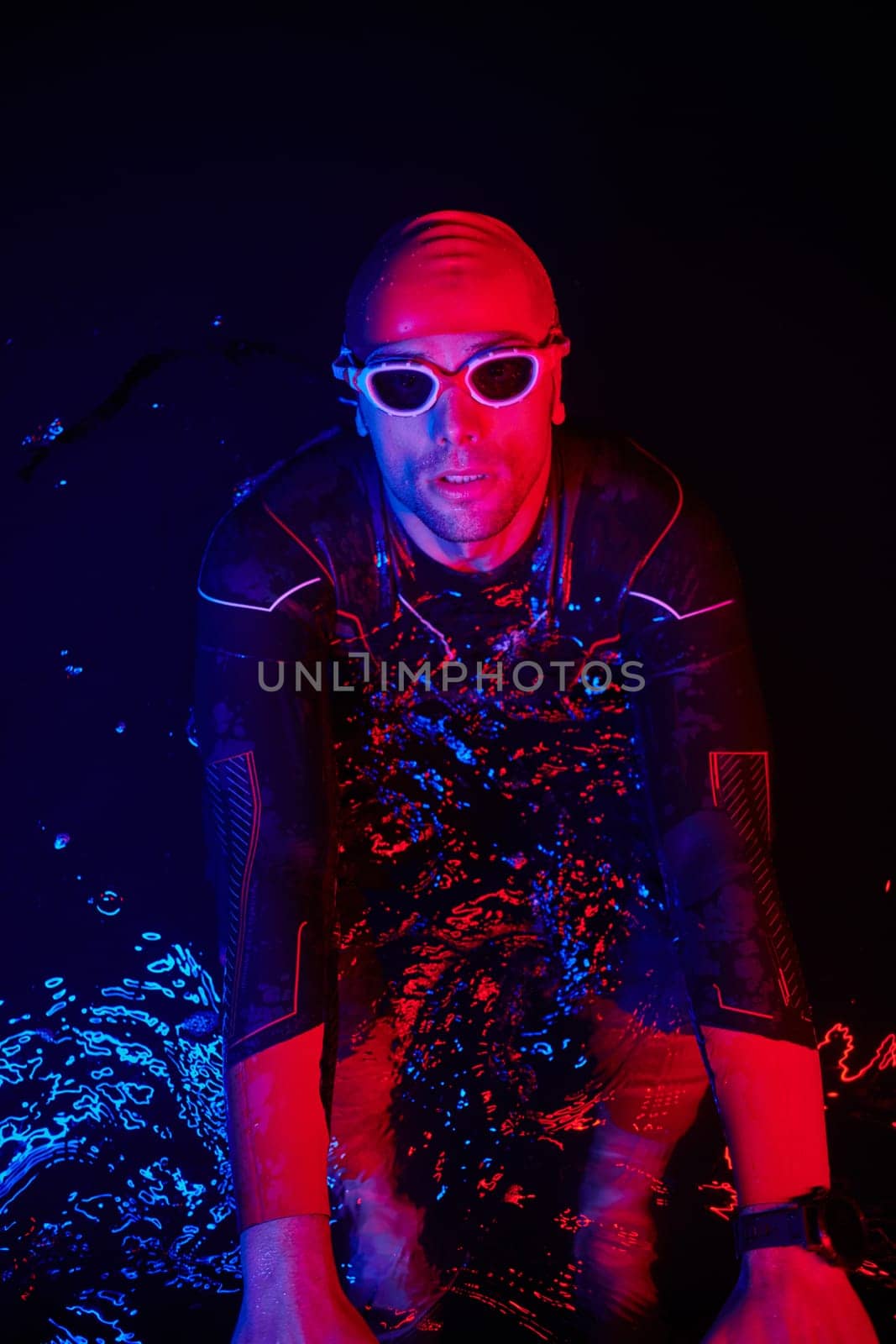 authentic triathlete swimmer having a break during hard training on night neon gel light by dotshock