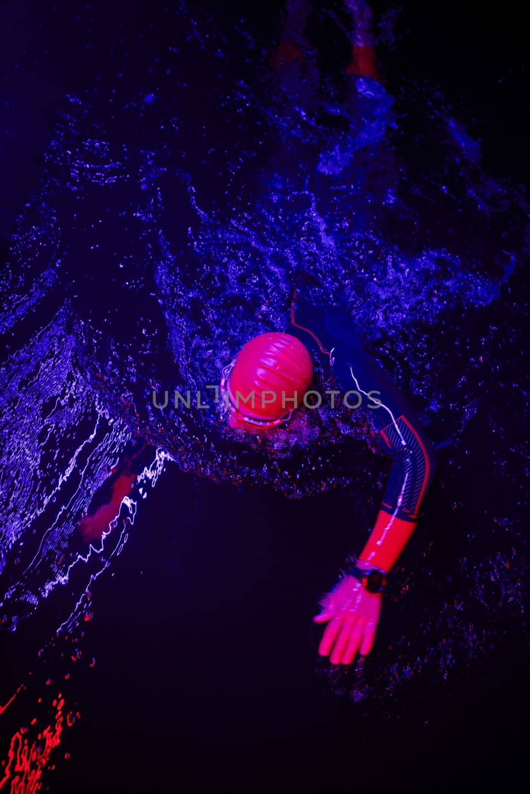 Authentic triathlete swimmer having a break during hard training on night neon gel light by dotshock