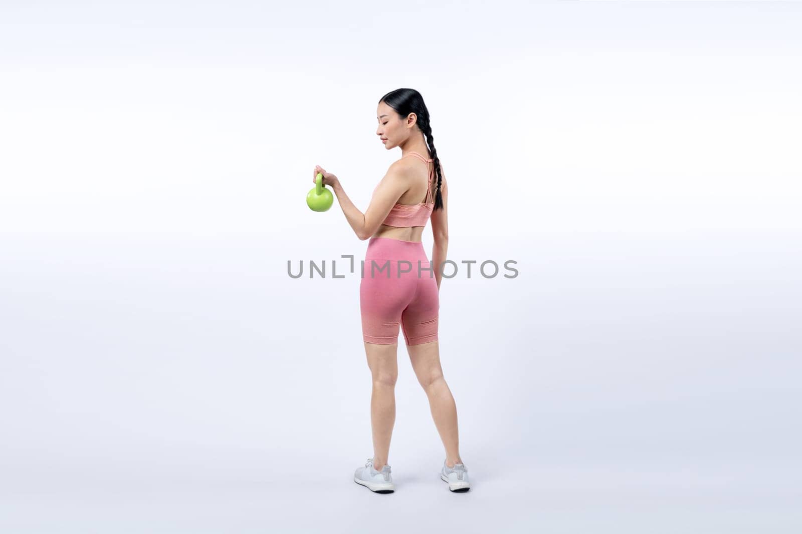 Vigorous energetic woman doing kettlebell weight lifting exercise on isolated background. Young athletic asian woman strength and endurance training session as body workout routine.