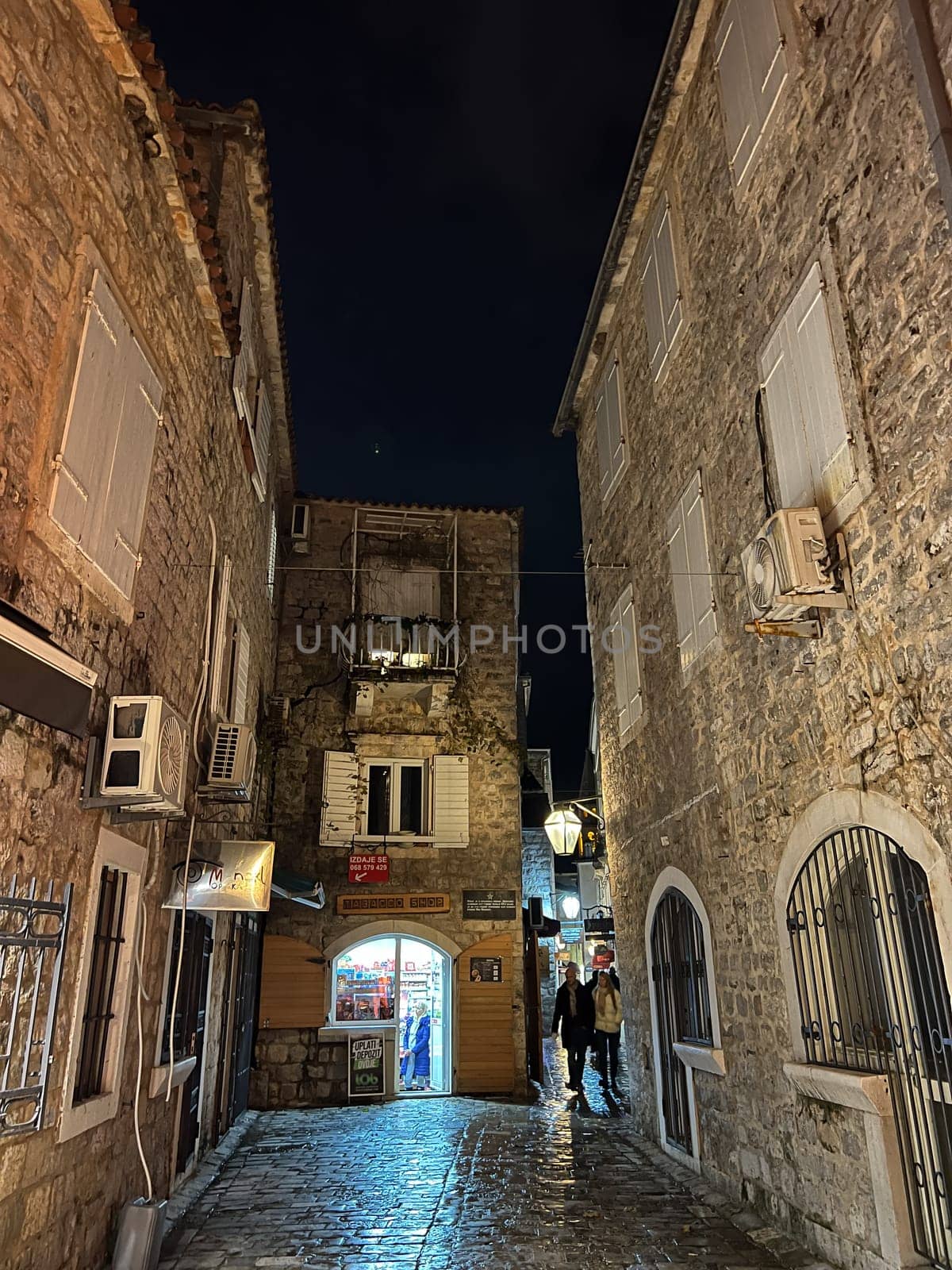 Budva, Montenegro - 25 december 2022: Narrow street of the ancient town illuminated by lanterns by Nadtochiy