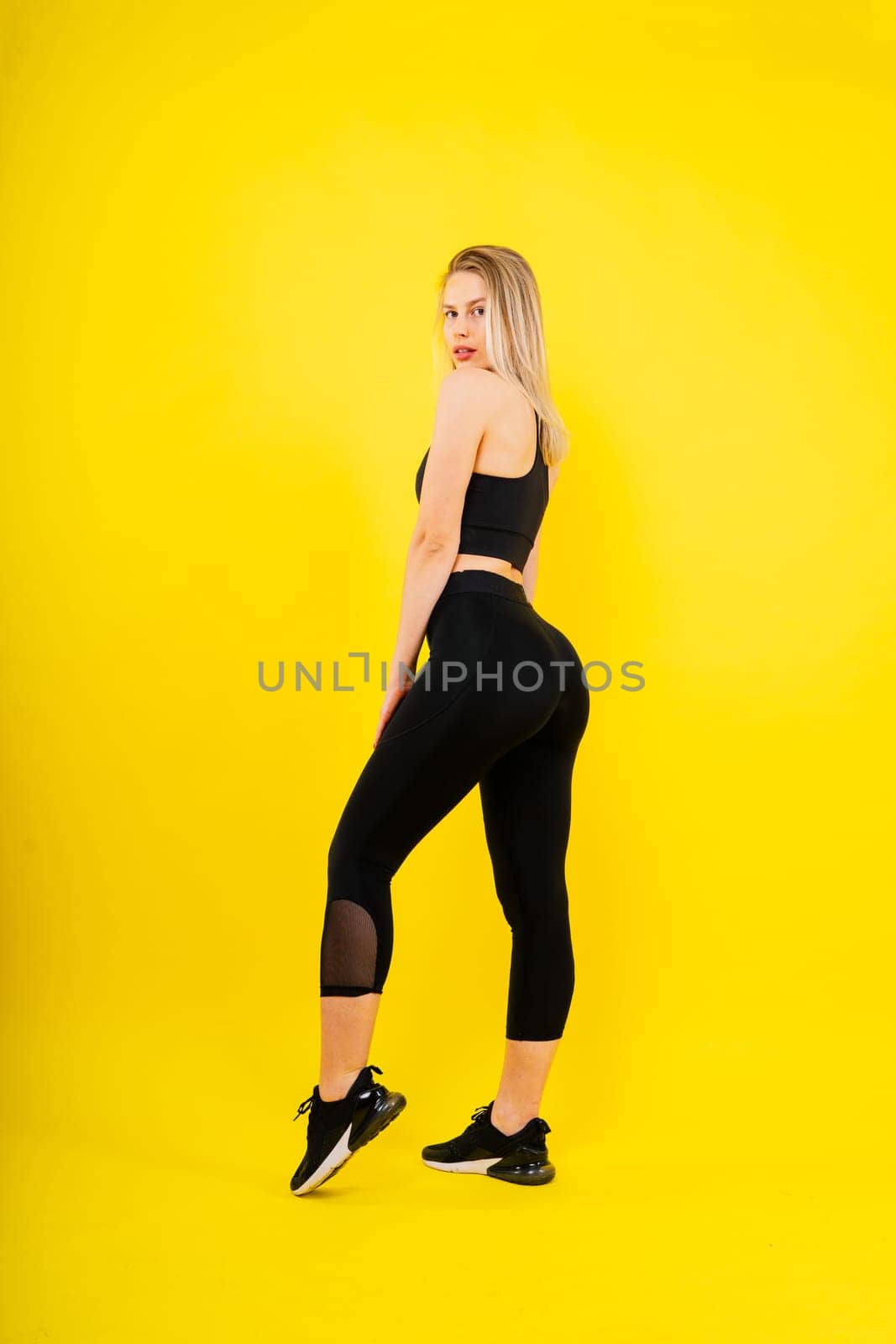 Beautiful young woman dressed in sports uniform, posing in studio on yellow red dark background.