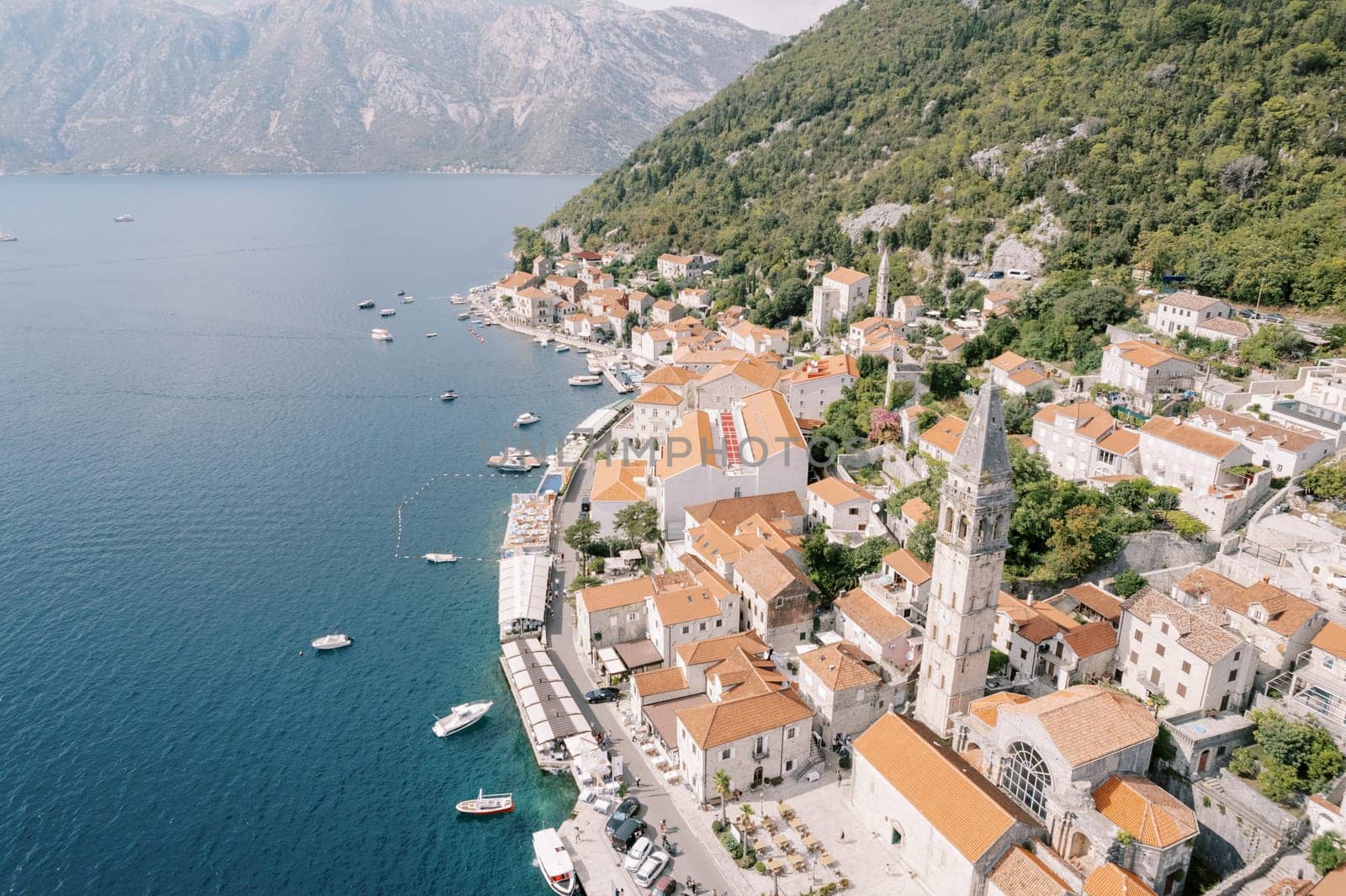 Moored boats off the coast of Perast with the high bell tower of the Church of St. Nicholas among ancient houses. Montenegro. Drone. High quality photo