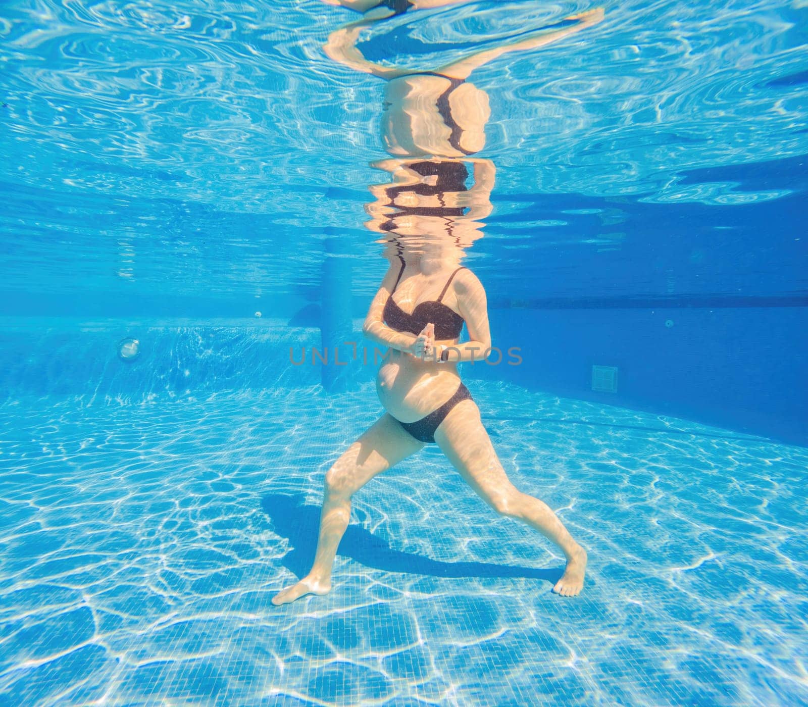 Embracing aquatic fitness, a pregnant woman demonstrates strength and serenity in underwater aerobics, creating a serene and empowering image in the pool.