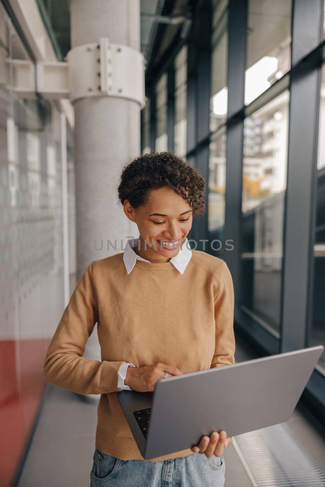 Smiling female manager using laptop while standing on modern office background by Yaroslav_astakhov