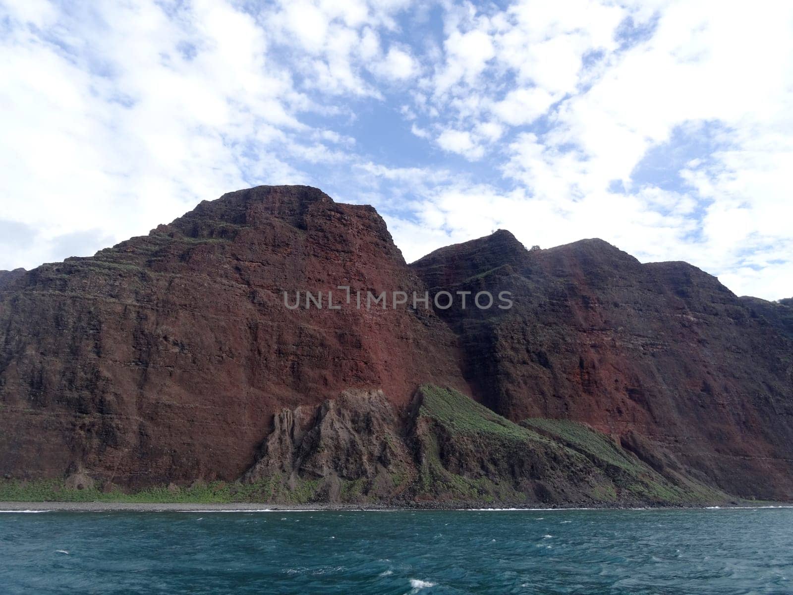 The Na Pali Coast on Kauai, a rugged and scenic stretch of coastline with red cliffs, green vegetation, and blue ocean.