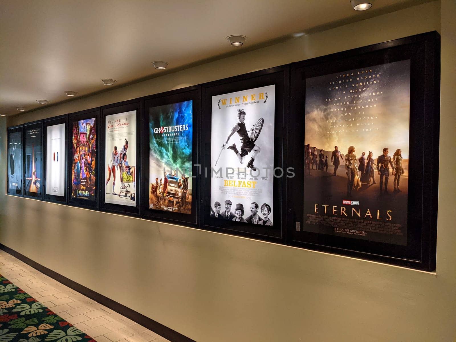 Honolulu - November 5, 2021: row of movie posters for upcoming releases in Kahala Mall, a shopping center in Honolulu, Hawaii. The photo shows the posters for the movies "Ghostbusters: Afterlife", "Belfast", "The Eternals", "King Richard", and "Encanto". The photo is taken from a close-up angle, focusing on the posters and the frames.