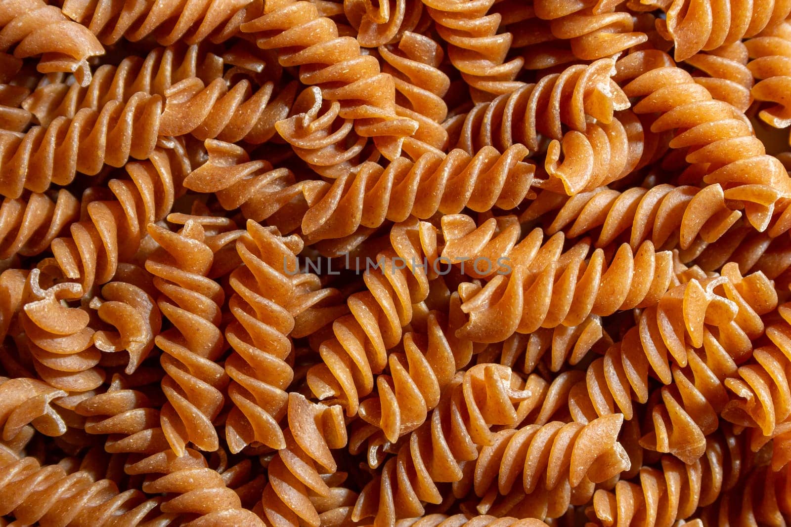 Uncooked Whole Grain Fusilli Pasta Background by InfinitumProdux
