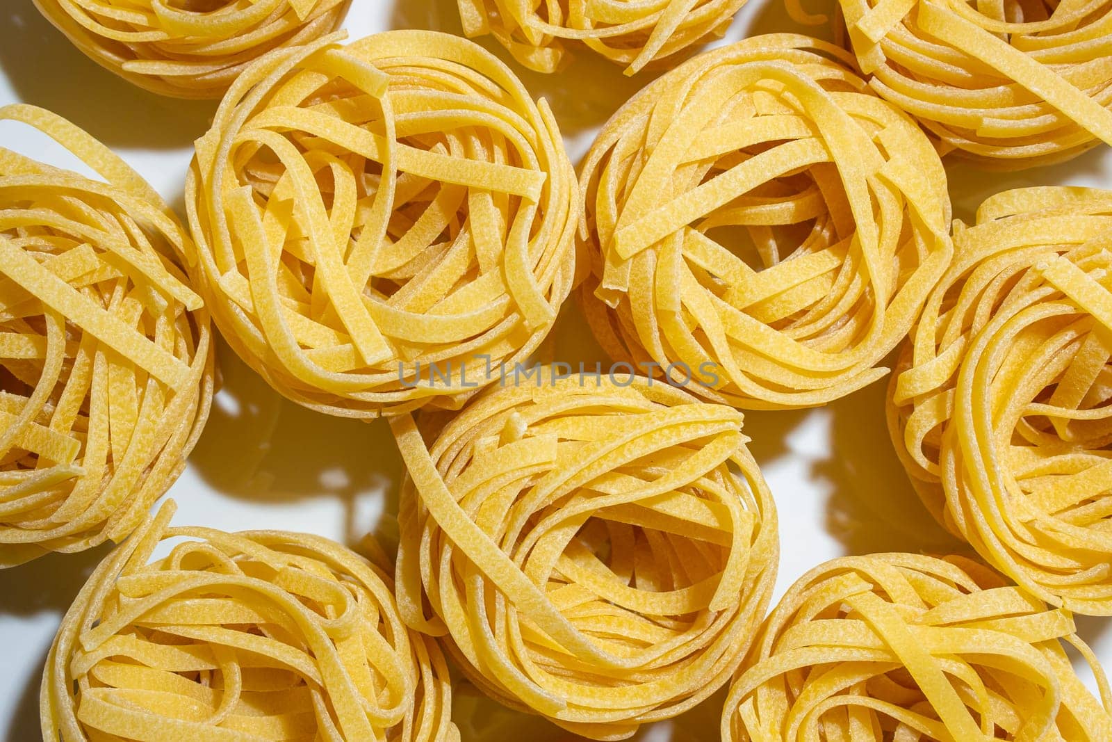 Uncooked Egg-Based Fettuccine Pasta: A Culinary Canvas of Ribbon-Shaped Macaroni, Creating a Lively and Textured Background for Gourmet Cooking. Dry Pasta. Raw Macaroni - Top View, Flat Lay