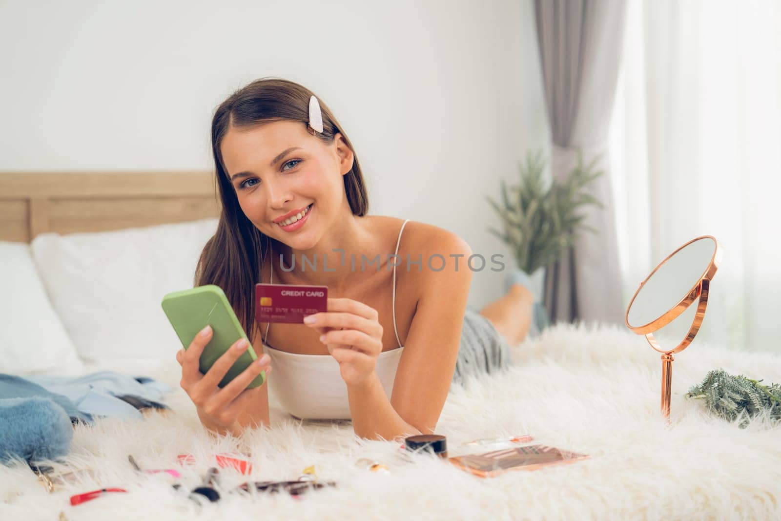 Young woman lying on bed using online payment app. Unveiling by biancoblue